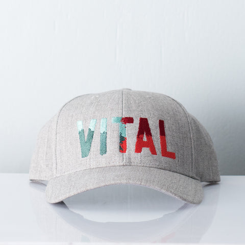 Grey melange hat embroidered with Vital Camo - a colorful logo displaying light blue, teal, electric red and maroon