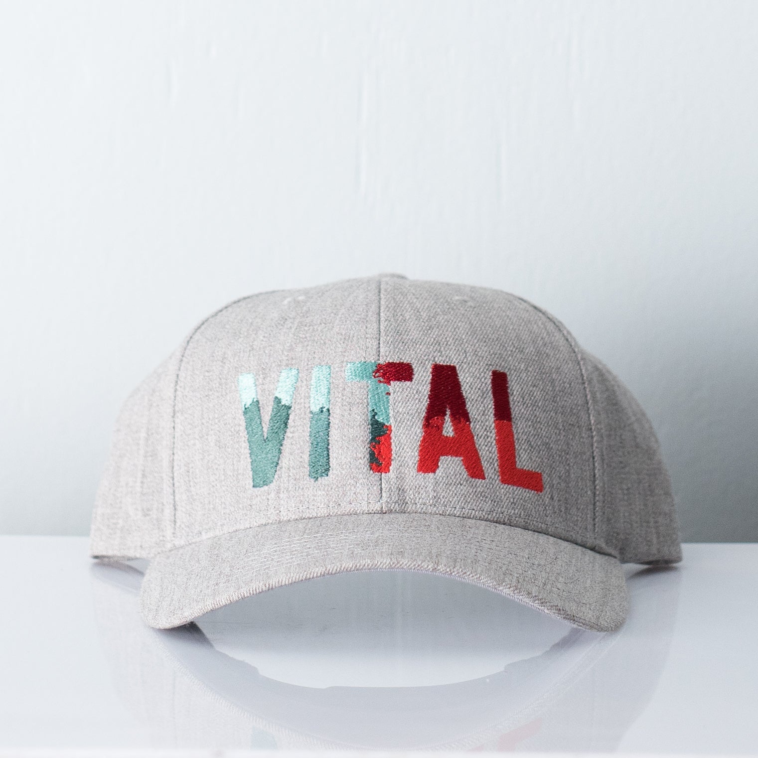 Grey melange hat embroidered with Vital Camo - a colorful logo displaying light blue, teal, electric red and maroon